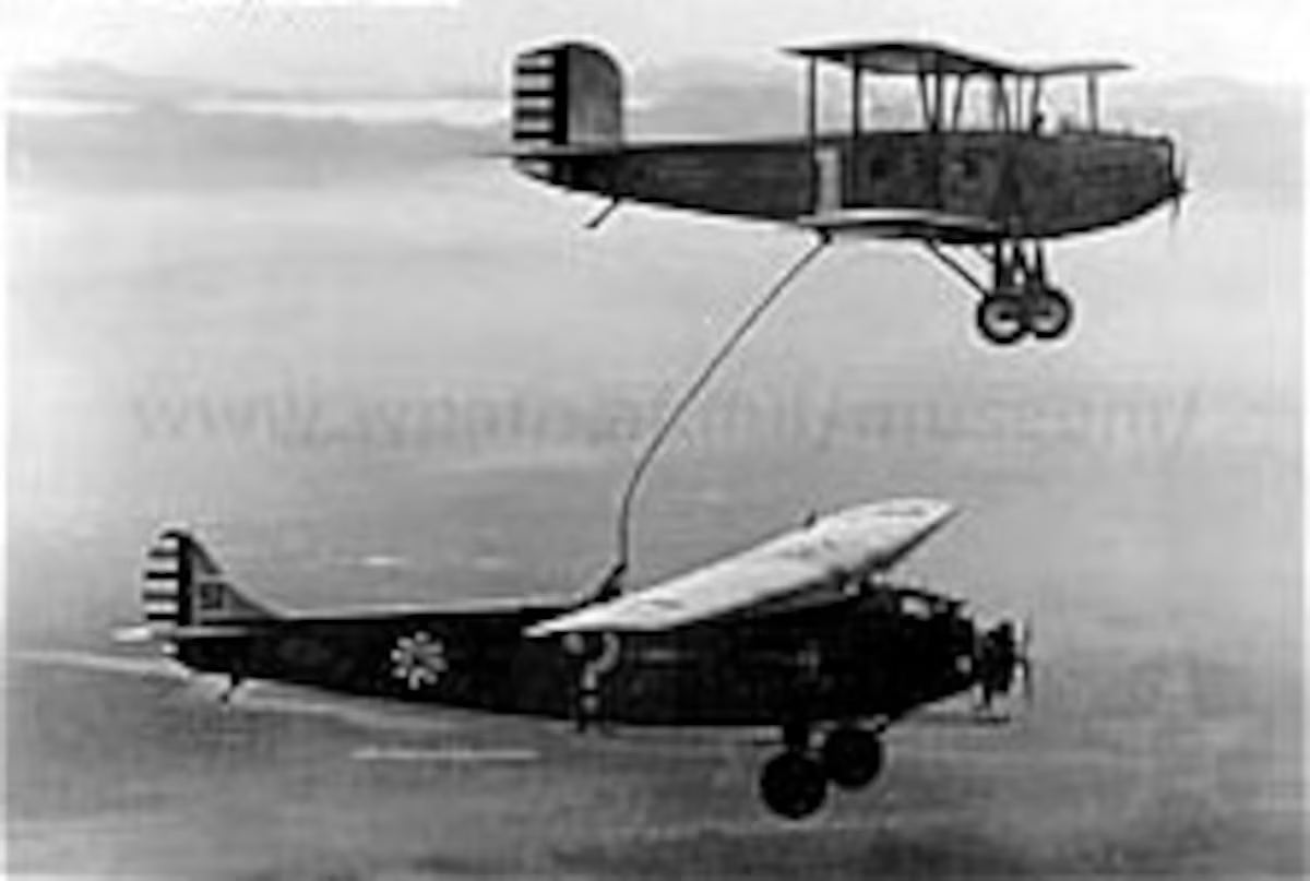 Two biplanes in flight, one passing a refueling hose to the Question Mark below, January 1929.